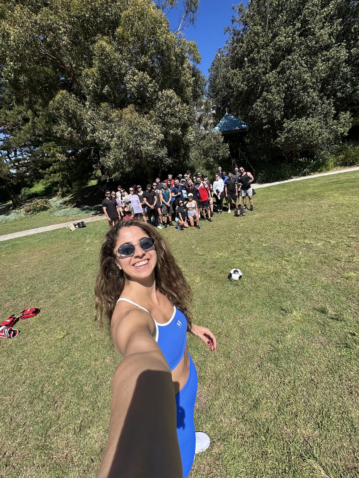 A large team gathered together after an MA Fitness event in a Sydney park, with boxing gloves and a ball on the grass